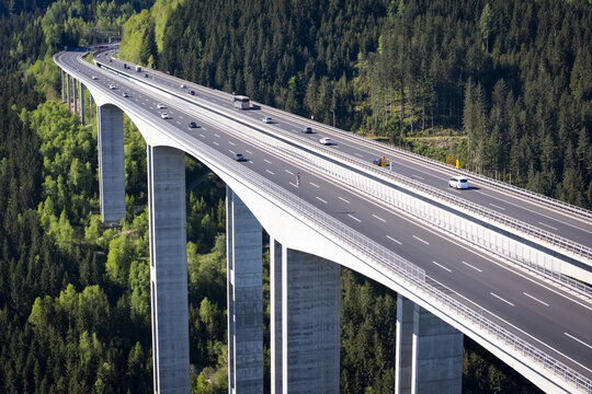 Aerial view of a towering viaduct slicing through a dense forest, as vehicles traverse its smooth asphalt surface, Wolfsberg, Carinthia, Austria.