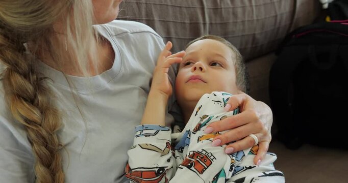 Sick preschooler boy communicates touching mother face while measuring temperature. Blonde woman with braid takes care of little ill son at home