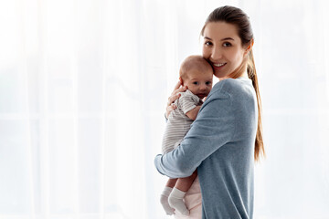 Young Loving Mother Caring Her Newborn Baby While Standing Near Window At Home, Portrait Of Happy...