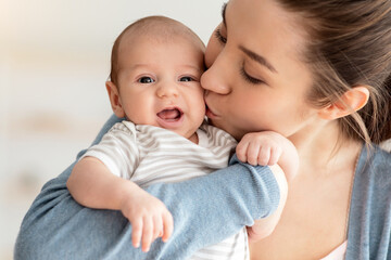 Mother's Love. Closeup Portrait Of Young Mom Kissing Her Cute Few Month Old Newborn Child, Loving Mum Bonding With Infant Baby At Home, Millennial Woman Enjoying Motherhood And Maternity Leave,