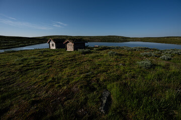 Boathouse and lake lit by the low sun on a Norwegian summer morning in the highlands, Vågå,...