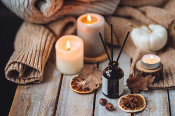 Concept of house decor, apartment seasonal fragrance. Thanksgiving. Autumn mood, cozy fall home atmosphere. Aroma diffuser, pumpkins, knitted warm sweaters, burning candles, dry leaves on wooden table