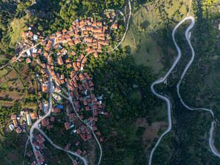 Drone photo showing Gelemiç village spread across sloped terrain with winding roads, cultivated...