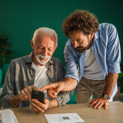 Adult mature son helping senior father using smart phone at home