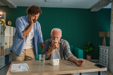 Worried son checking blood pressure of his sick senior father at home
