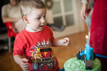 A young child in a red shirt stares with excitement at a green birthday cake adorned with a small...