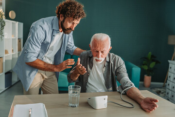 Worried son checking blood pressure of his sick senior father at home