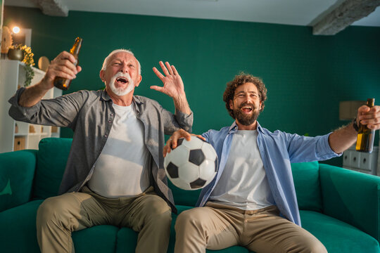 Father and son celebrating goal while watching soccer match at home - Powered by Adobe