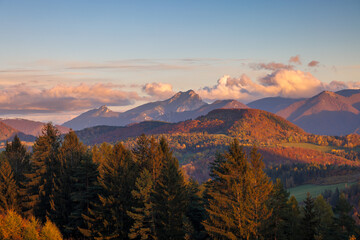 Obraz premium Autumnal mountain landscape with warm light highlighting trees and peaks against a blue, cloudy sky. The Mala Fatra national park in Slovakia, Europe.