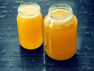 Two glass jars of golden bee honey are on a wet table, green grass field and sky in the background. Fine organic product concept. Agriculture and food industry.