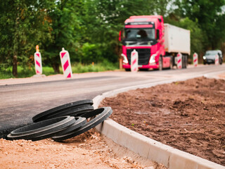Road works in a rural country side area. Plastic fittings and freshly laid asphalt in foreground,...