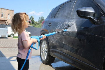 Young girl helping wash a car with foam at a self-service car wash on a warm sunny day