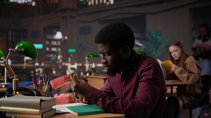 African american student examining fake teeth for dentistry thesis, working on stomatology research with appropriate tools in the campus library. Guy preparing for his career. Camera B.