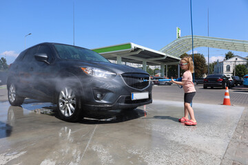 Young girl helping wash a car with foam at a self-service car wash on a warm sunny day