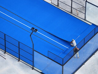 Top view of two workers installing bright blue sports court flooring with a white line marking

