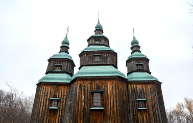 Distinctive wooden architecture of a Ukrainian church, featuring three prominent domes with teal...
