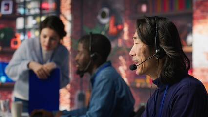 Call center agent speaking in audio headset microphone, using remote access tools. Worker in...