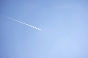 High-altitude airplane leaving contrail in clear blue sky, minimal composition with space for text or travel concept visuals