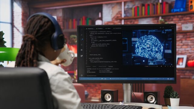 Software developer wearing headphones using computer at home for artificial intelligence computing simulating human brain. IT expert listening music and working with AI deep neural networks, camera B