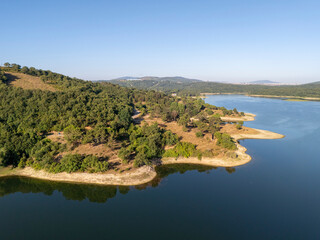 Obraz premium Scenic aerial view of Ömerli Dam featuring calm waters, lush green forests, and curved shorelines under a bright blue sky, ideal for nature, landscape, and environmental themed stock use. 