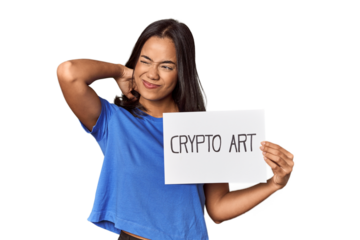 Woman with "crypto art" sign in studio touching back of head, thinking and making a choice.