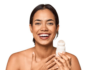 Filipino woman holds deodorant in studio laughs out loudly keeping hand on chest.