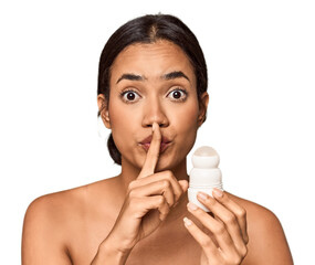 Filipino woman holds deodorant in studio keeping a secret or asking for silence.