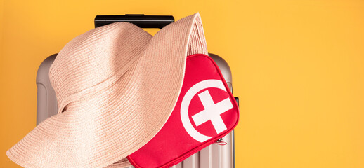 Safe travel concept. Light brown suitcase, big hat and red first aid kit on bright yellow...