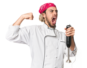 Young Caucasian chef using mixer in studio raising fist after a victory, winner concept.