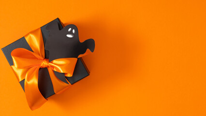 Colorful Halloween background with paper ghost figures and black elegant gift and orange ribbon on...