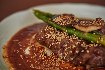 A Savory Dish Featuring Succulent Beef Topped with Grilled Asparagus, Mushrooms, and a Garnish of Toasted Sesame Seeds in a Rich Sauce