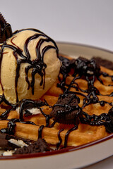 A decadent dessert featuring crispy waffles topped with creamy vanilla ice cream, drizzled with...