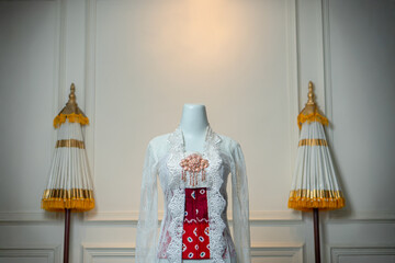 Traditional Indonesian bridal gown with elegant white lace kebaya and red batik, designed for a...