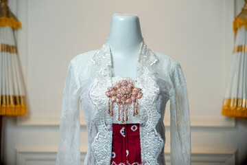 Close-up of a traditional Indonesian bridal kebaya with detailed white lace and ornate brooch,...