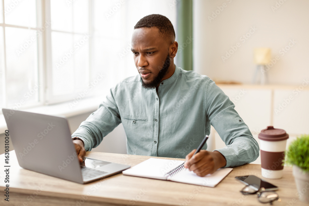 Poster serious black businessman working taking notes and using laptop computer writing business report at 