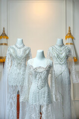 Three luxurious white bridal gowns with intricate lace, embroidery, and beaded details are elegantly displayed on mannequins, ideal for traditional akad nikah and wedding themes.
