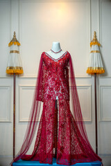 A luxurious red lace bridal gown with intricate floral details and elegant transparent sleeves, displayed on a mannequin in a classic, formal setting.