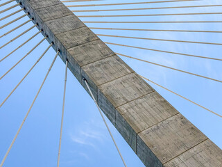 Obraz premium Cables on a suspension bridge connected to a cement anchor column on a blue sky day