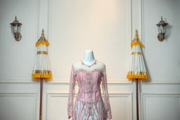 A detailed pink bridal gown displayed on a mannequin, embellished with beads and sequins, placed in...