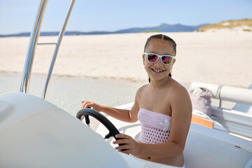 Young girl steering a boat in bright sunshine on a sandy beach during summer vacation fun