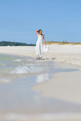 Woman in white dress walking along tranquil beach on sunny day