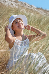 Young girl enjoys sunshine in a field, wearing a white dress and sun hat on a clear day