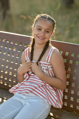 Young girl with braids smiling on a park bench during a sunny afternoon in a nature setting