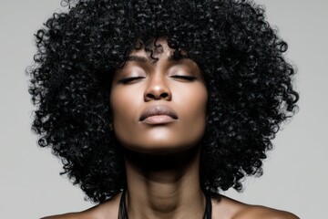 Fototapeta premium Captivating portrait of a serene woman with voluminous curly hair radiating confidence under studio lighting emphasizing powerful beauty and individual identity in a minimalist setting