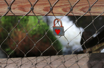 Heart-Shaped Padlock on Wire Fence with Greenery and Waterfall Background