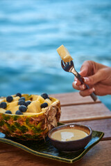 A Refreshing Tropical Delight: Enjoying Fresh Pineapple Slices Topped with Juicy Blueberries and a Creamy Dip by the Water's Edge