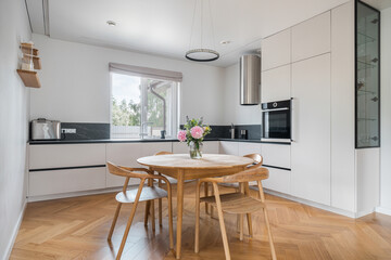 Modern kitchen interior featuring a round wooden table with flowers and stylish decor during daylight