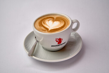A Beautifully Crafted Latte with an Intricate Heart Design Served in a Classic White Cup on a Stylish Plate with a Spoon