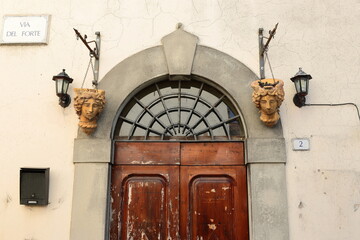 Sconces and hanging planters on both sides of a Renaissance-style, round arch wood door on Via del...