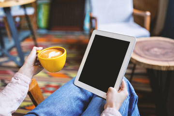 Modern lifestyle concept. Unrecognizable lady holding digital tablet with black screen and drinking coffee, sitting at table in cafeteria. Mockup for your design or website.